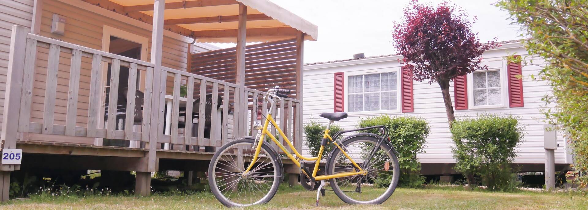 un vélo jaune et noir est garé grace à sa béquille sur l'herbe devant un grand mobilhome de camping